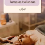 A imagem mostra uma mulher deitada em uma mesa de massagem em um ambiente tranquilo, com um terapeuta realizando atendimento. A luz suave e o ambiente acolhedor evocam sentimentos de paz e relaxamento. Esta imagem capta a essência das terapias holísticas, destacando a interação humana e o ambiente curativo, além de atrair visualmente o público predominantemente feminino do artigo.
